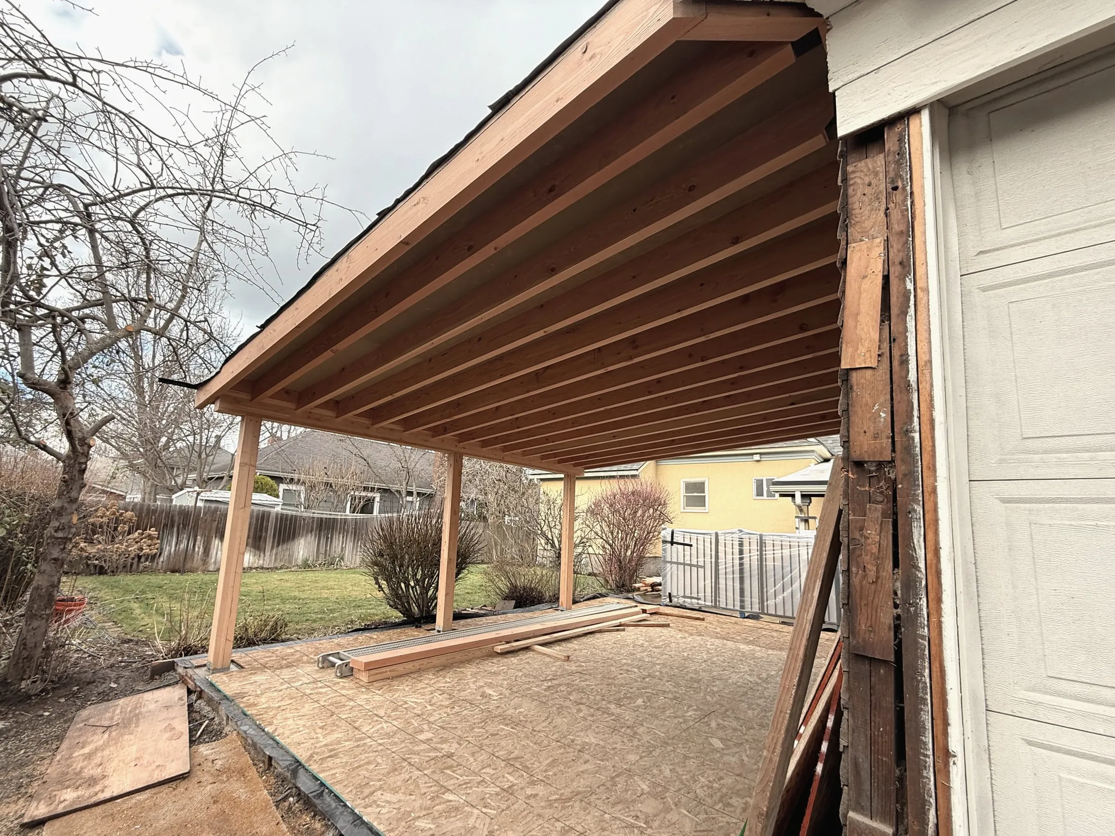 Under the new roof looking out at the yard — rafters overhead, posts at the edge of the deck